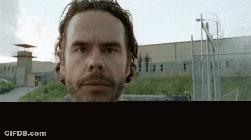 A Man With A Beard And A Tattoo On His Face Is Standing In Front Of A Prison Building . GIF