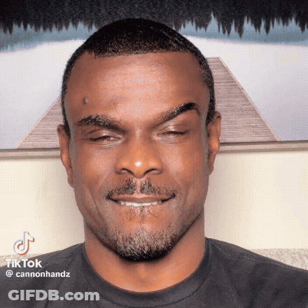 A Man With A Beard And A Tattoo On His Forehead Is Smiling And Looking At The Camera .. GIF