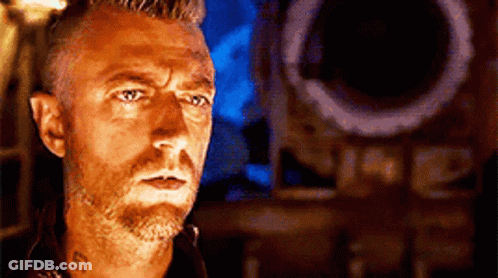 A Man With A Beard And A Tattoo On His Neck Is Standing In Front Of A Speaker . GIF