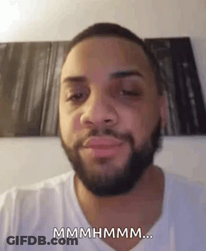 A Man With A Beard And A White Shirt Is Making A Funny Face And Saying Mmmmhmm . GIF