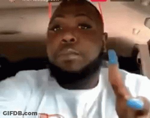 A Man With A Beard And A White Shirt Is Sitting In A Car Holding A Blue Object . GIF