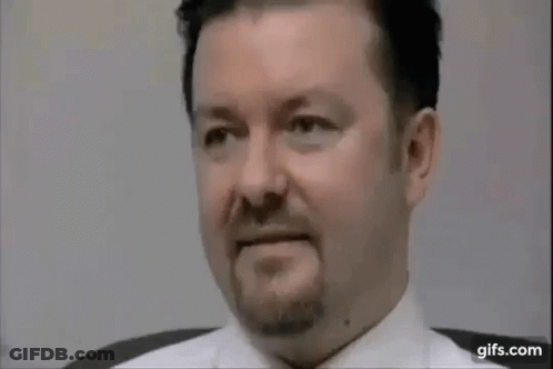 A Man With A Beard And A White Shirt Is Sitting In A Chair . GIF