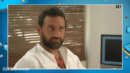 A Man With A Beard And A White Shirt Is Sitting In Front Of A Window With Blinds . GIF