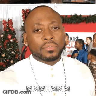 A Man With A Beard And A White Shirt Is Standing In Front Of A Christmas Tree . GIF