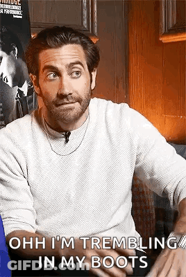 A Man With A Beard And A White Sweater Is Sitting On A Couch And Talking To Someone . GIF