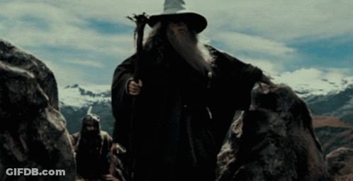 A Man With A Beard And A Wizard Hat Is Walking Through A Rocky Area GIF