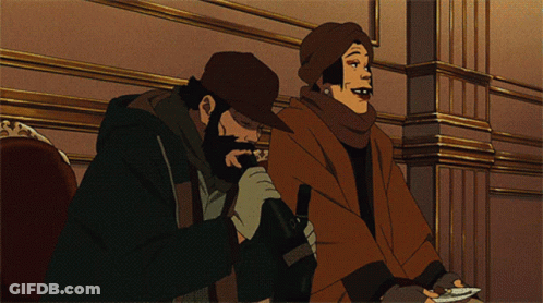 A Man With A Beard And A Woman With A Scarf Around Their Neck Are Sitting Next To Each Other GIF