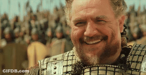 A Man With A Beard And Armor Is Smiling In Front Of A Crowd Of People . GIF
