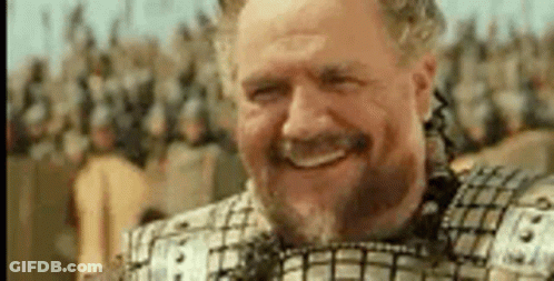 A Man With A Beard And Armor Is Smiling In Front Of A Crowd Of Soldiers . GIF