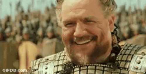 A Man With A Beard And Armor Is Smiling In Front Of A Crowd . GIF
