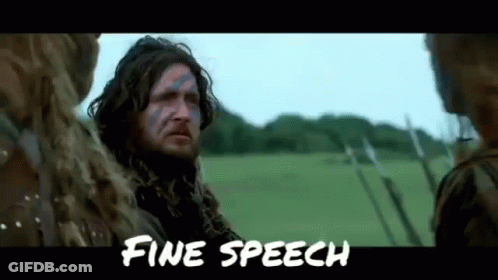 A Man With A Beard And Blue Paint On His Face Is Standing In A Field With Other People . GIF