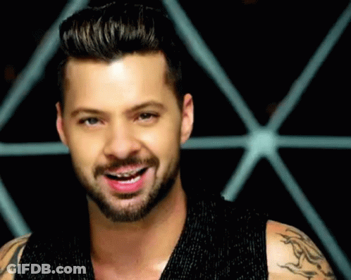 A Man With A Beard And Braces On His Teeth Is Smiling In Front Of A Geometric Pattern . GIF