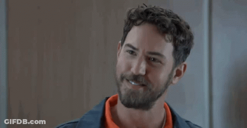 A Man With A Beard And Curly Hair Is Smiling While Wearing An Orange Shirt . GIF