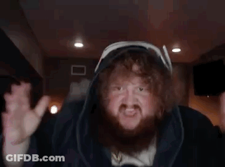 A Man With A Beard And Curly Hair Is Wearing A Hooded Jacket And Making A Funny Face . GIF