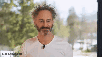A Man With A Beard And Curly Hair Is Wearing A White T-Shirt And A Microphone . GIF