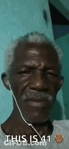 A Man With A Beard And Ear Buds Is Wearing Headphones . GIF