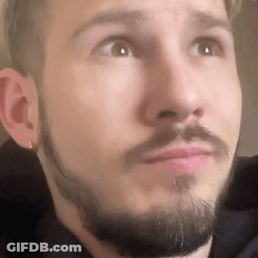A Man With A Beard And Earrings Is Looking Up At The Camera . GIF