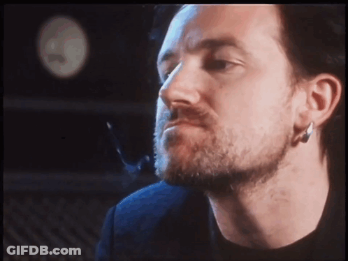 A Man With A Beard And Earrings Looks At The Camera GIF