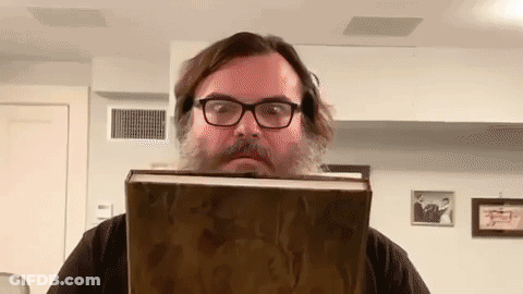 A Man With A Beard And Glasses Is Holding A Large Book In Front Of His Face . GIF