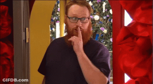 A Man With A Beard And Glasses Is Holding His Finger To His Lips GIF