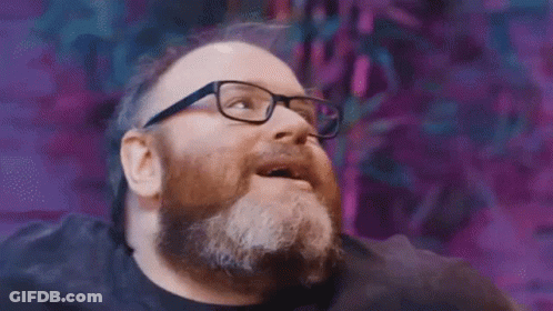 A Man With A Beard And Glasses Is Looking Up And Smiling . GIF