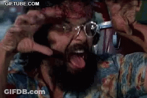 A Man With A Beard And Glasses Is Screaming With His Tongue Hanging Out . GIF