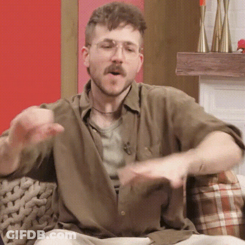 A Man With A Beard And Glasses Is Sitting On A Couch And Making A Funny Face . GIF