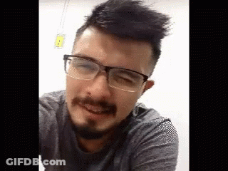 A Man With A Beard And Glasses Is Smiling And Looking At The Camera . GIF