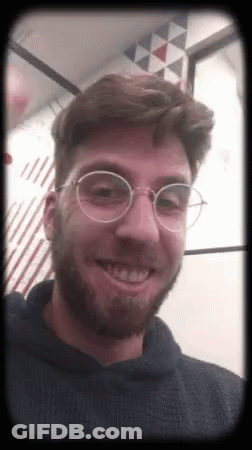 A Man With A Beard And Glasses Is Smiling And Wearing A Black Hoodie . GIF