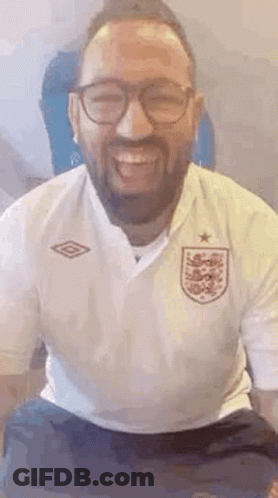A Man With A Beard And Glasses Is Smiling And Wearing A White Shirt . GIF