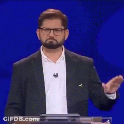 A Man With A Beard And Glasses Is Standing At A Podium With His Hands Outstretched . GIF