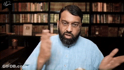 A Man With A Beard And Glasses Is Standing In Front Of A Bookshelf And Talking . GIF