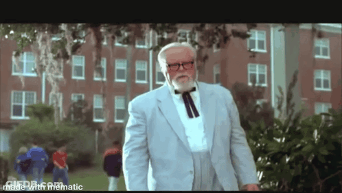 A Man With A Beard And Glasses Is Standing In Front Of A Brick Building . GIF