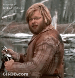 A Man With A Beard And Glasses Is Standing In The Woods Holding A Steering Wheel . GIF