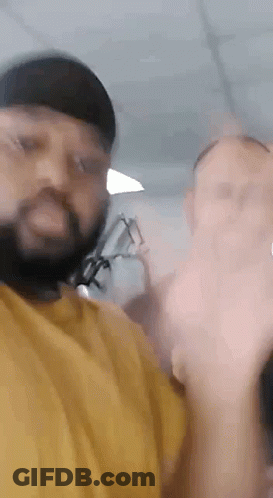 A Man With A Beard And Glasses Is Standing Next To A Woman In A Yellow Shirt . GIF