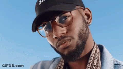 A Man With A Beard And Glasses Is Wearing A Baseball Cap And A Denim Jacket . GIF