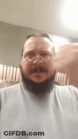A Man With A Beard And Glasses Is Wearing A White Shirt And Making A Funny Face . GIF