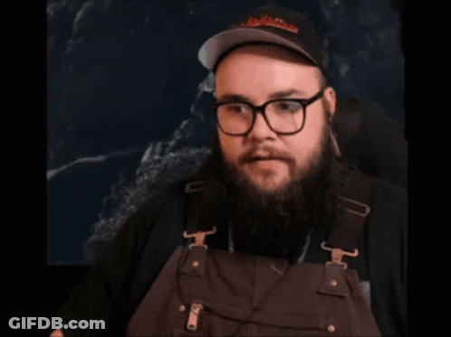 A Man With A Beard And Glasses Is Wearing Overalls And A Hat GIF