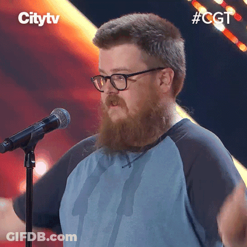 A Man With A Beard And Glasses Stands In Front Of A Microphone With The Hashtag #Cgt GIF