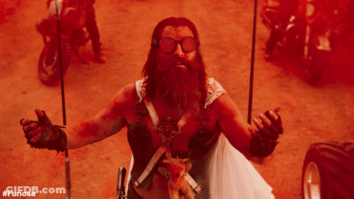 A Man With A Beard And Goggles Holds A Stuffed Animal In His Hand With The Hashtag #Furiosa On The Bottom Right GIF