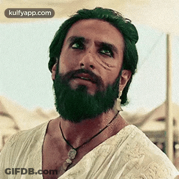 A Man With A Beard And Green Hair Is Wearing A Necklace And A White Shirt . GIF