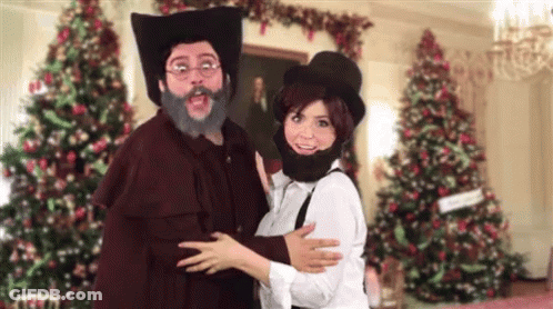 A Man With A Beard And Hat Is Hugging A Woman In Front Of Christmas Trees GIF