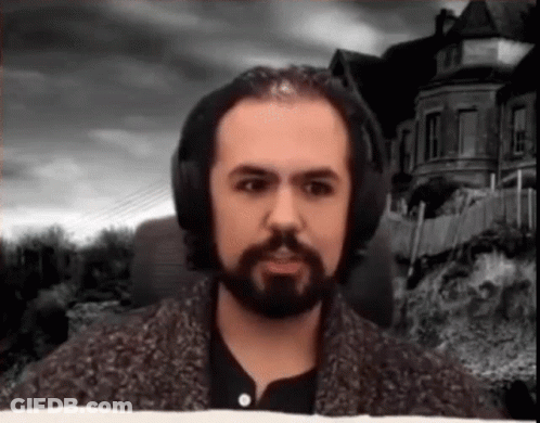 A Man With A Beard And Headphones Is Standing In Front Of A House . GIF