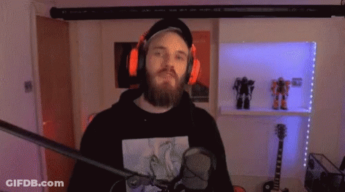 A Man With A Beard And Headphones Is Standing In Front Of A Microphone In A Room . GIF