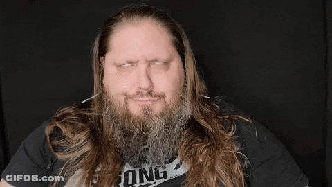 A Man With A Beard And Long Hair Is Wearing A Black Shirt And Making A Funny Face . GIF