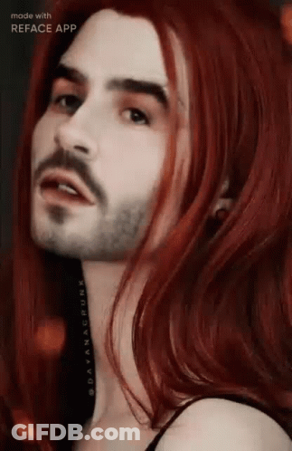 A Man With A Beard And Long Red Hair Is Looking At The Camera . GIF