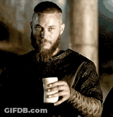 A Man With A Beard And Mustache Is Holding A Cup Of Coffee . GIF