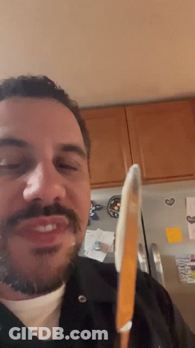 A Man With A Beard And Mustache Is Holding A Knife In Front Of A Refrigerator GIF