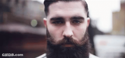 A Man With A Beard And Mustache Is Looking At The Camera With A Serious Look On His Face . GIF