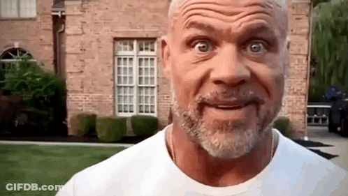 A Man With A Beard And Mustache Is Making A Funny Face In Front Of A Brick House . GIF